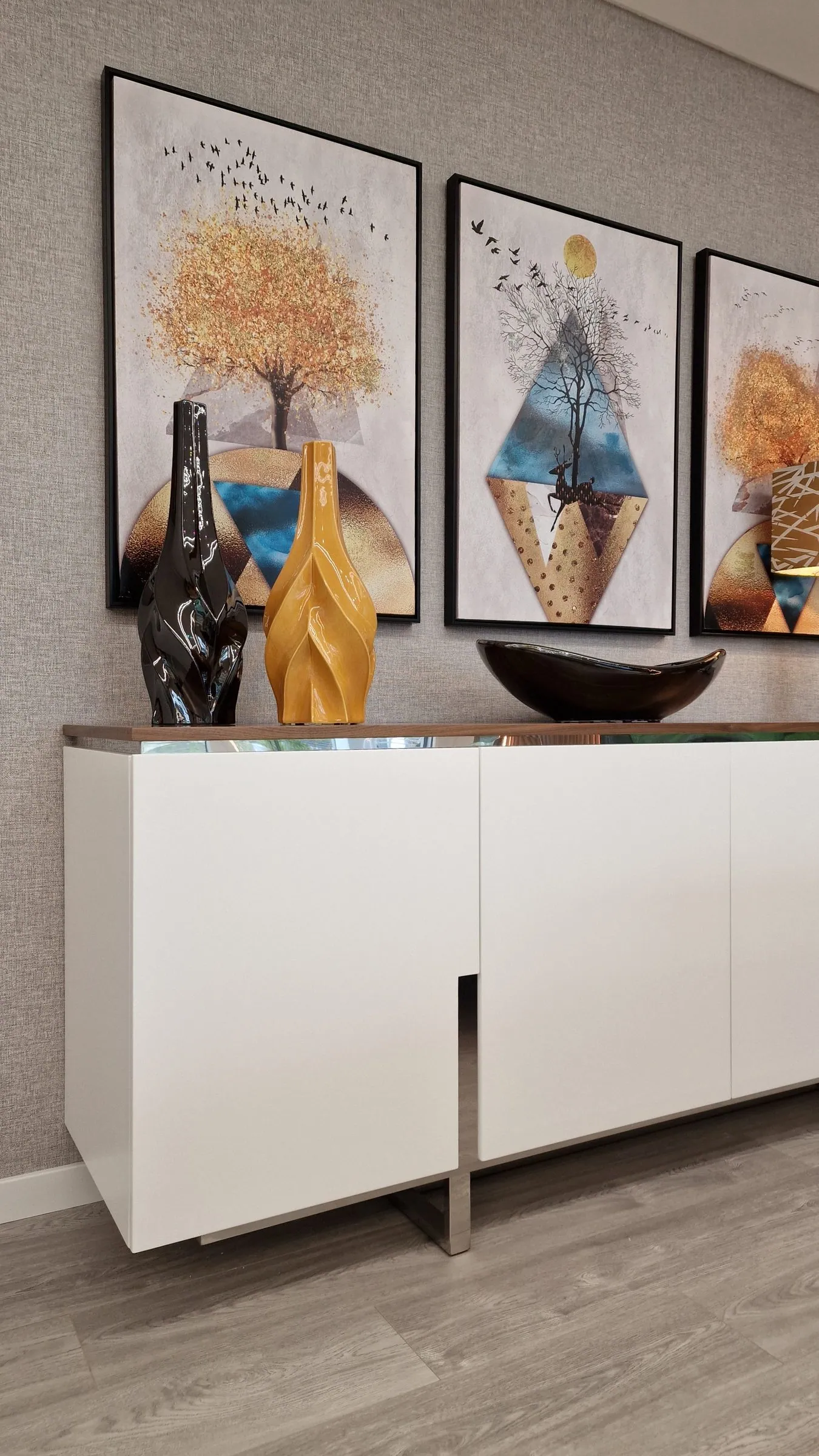 Aparador branco com três quadros e vasos decorativos.
