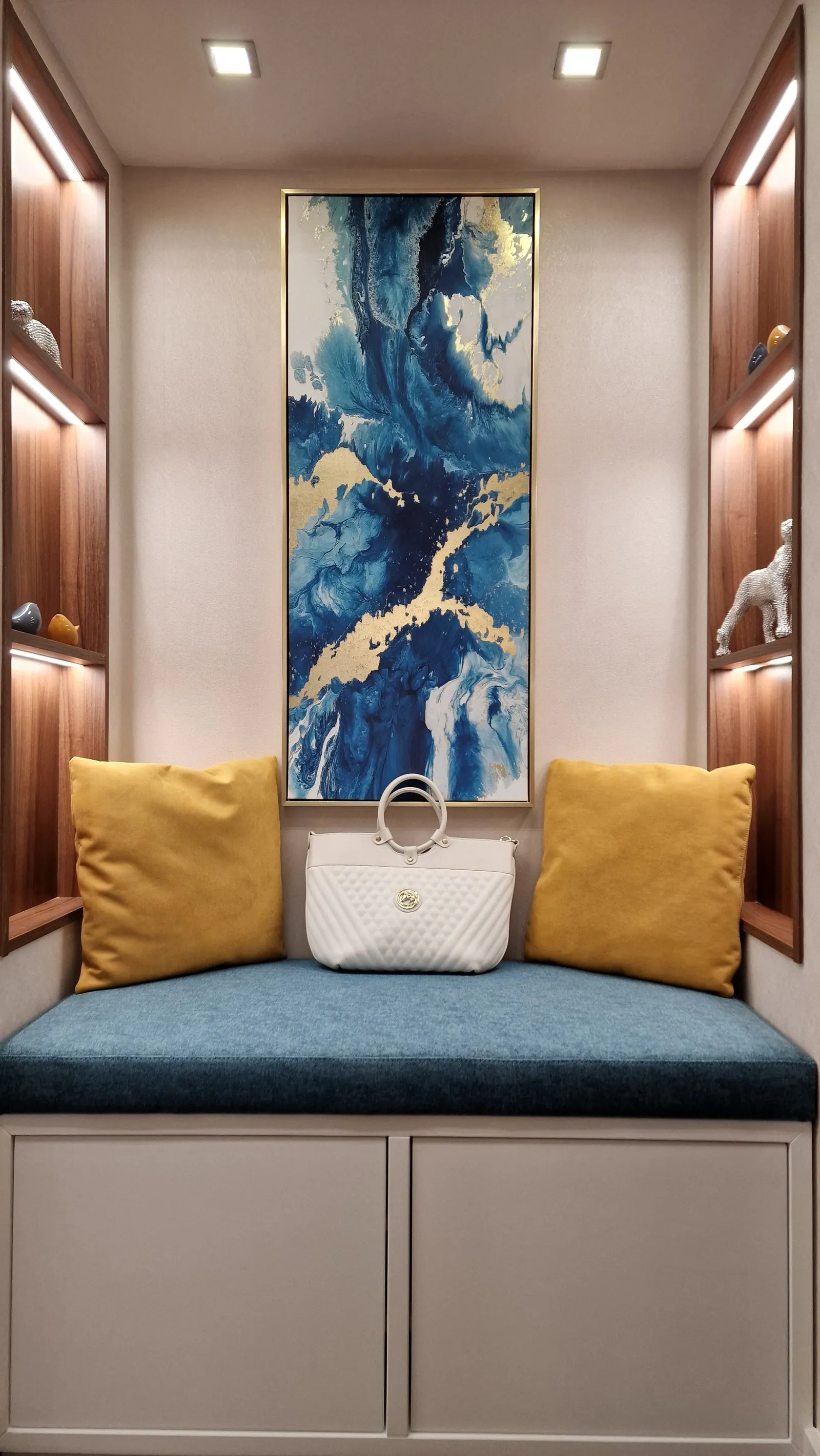 Banco embutido com almofadas, nicho iluminado e quadro azul.