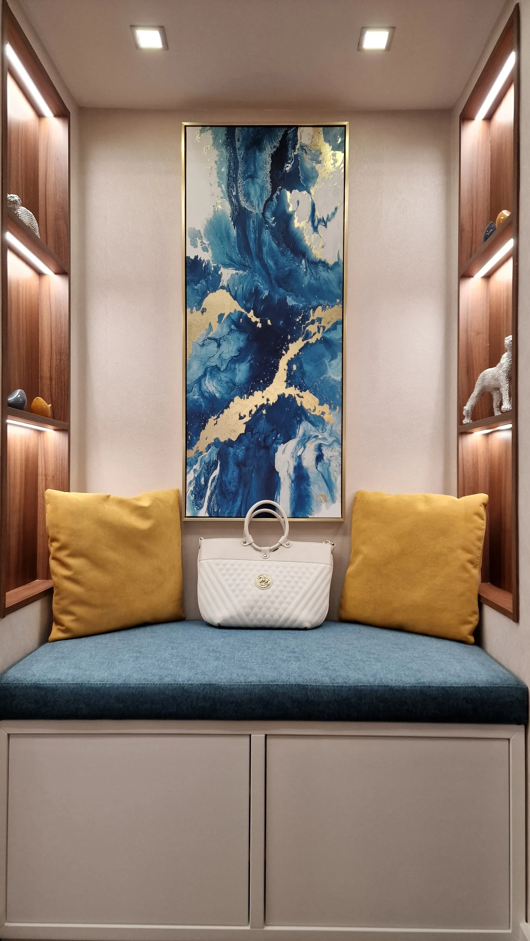 Banco embutido com almofadas, nicho iluminado e quadro azul.