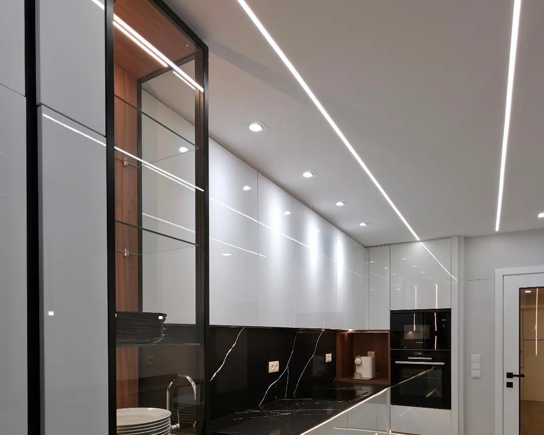 Cozinha com coluna de vidro e pedra negra, luz linear no teto.
