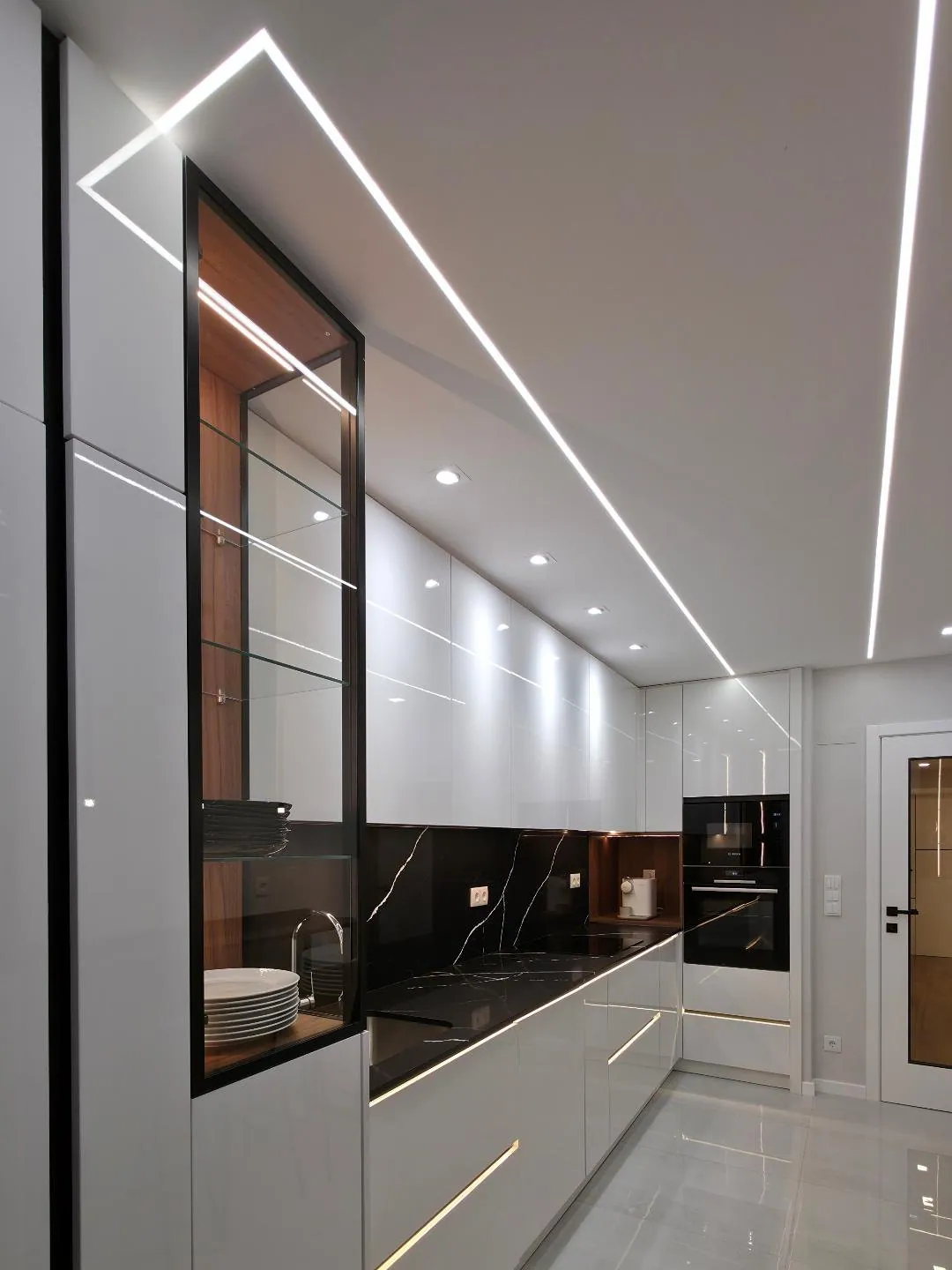 Cozinha com coluna de vidro e pedra negra, luz linear no teto.