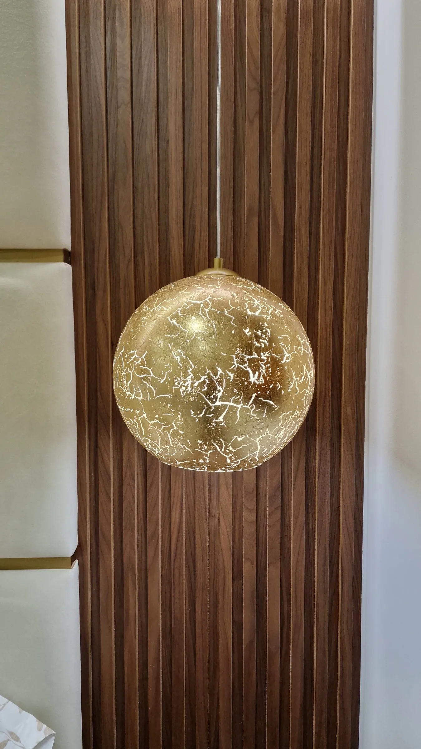 O candeeiro de globo dourado contra o ripado de madeira.