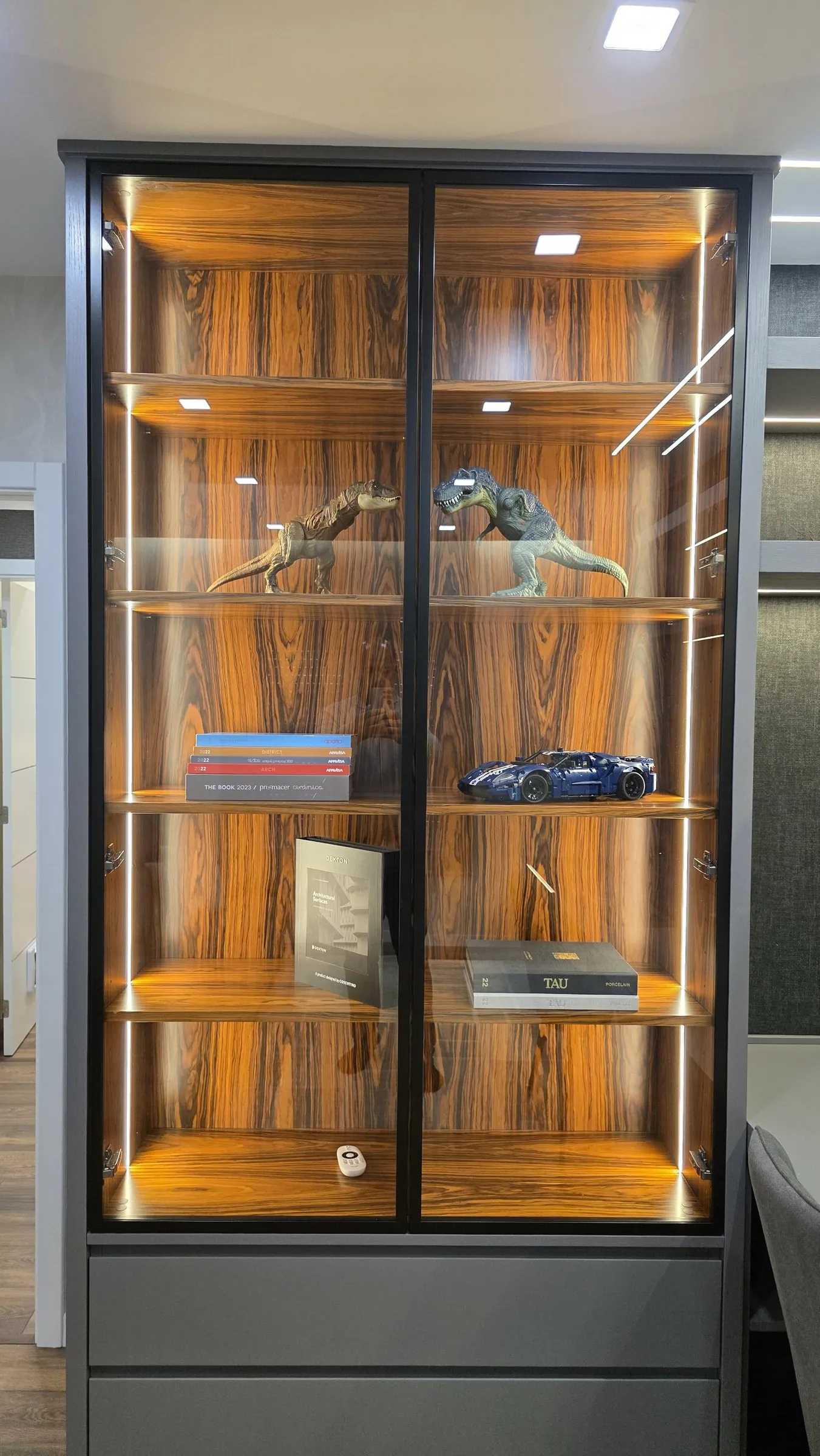 Vitrine com fundo em madeira de veio e prateleiras de vidro iluminadas.