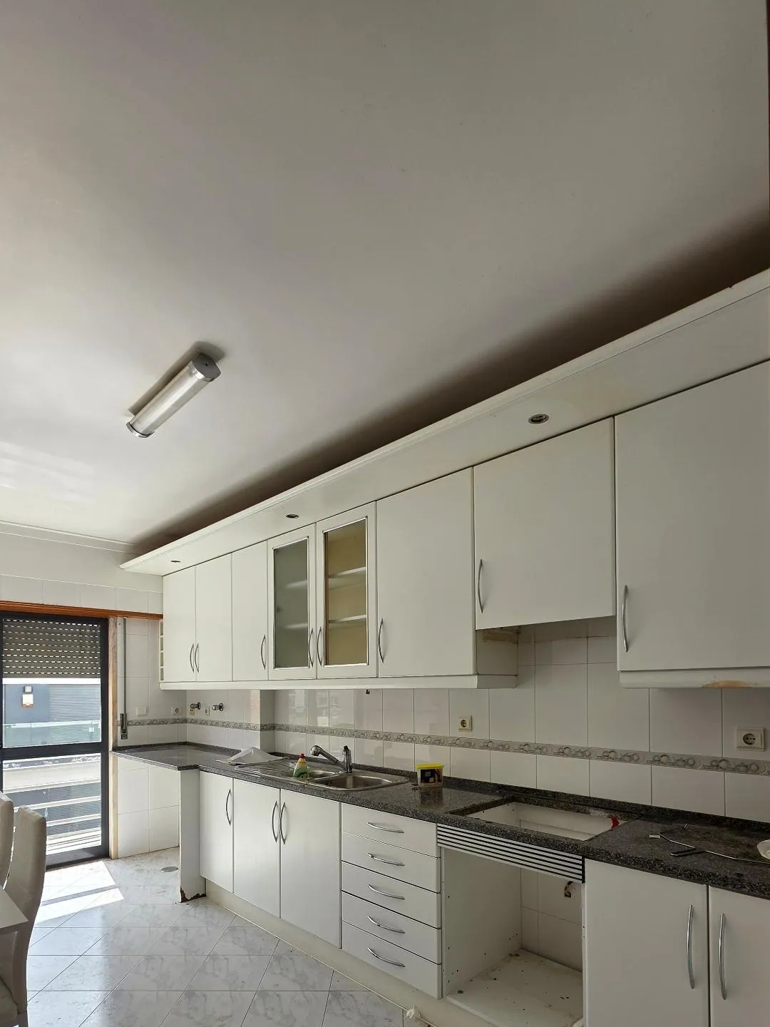 A cozinha antes, com armários brancos e bancada escura.