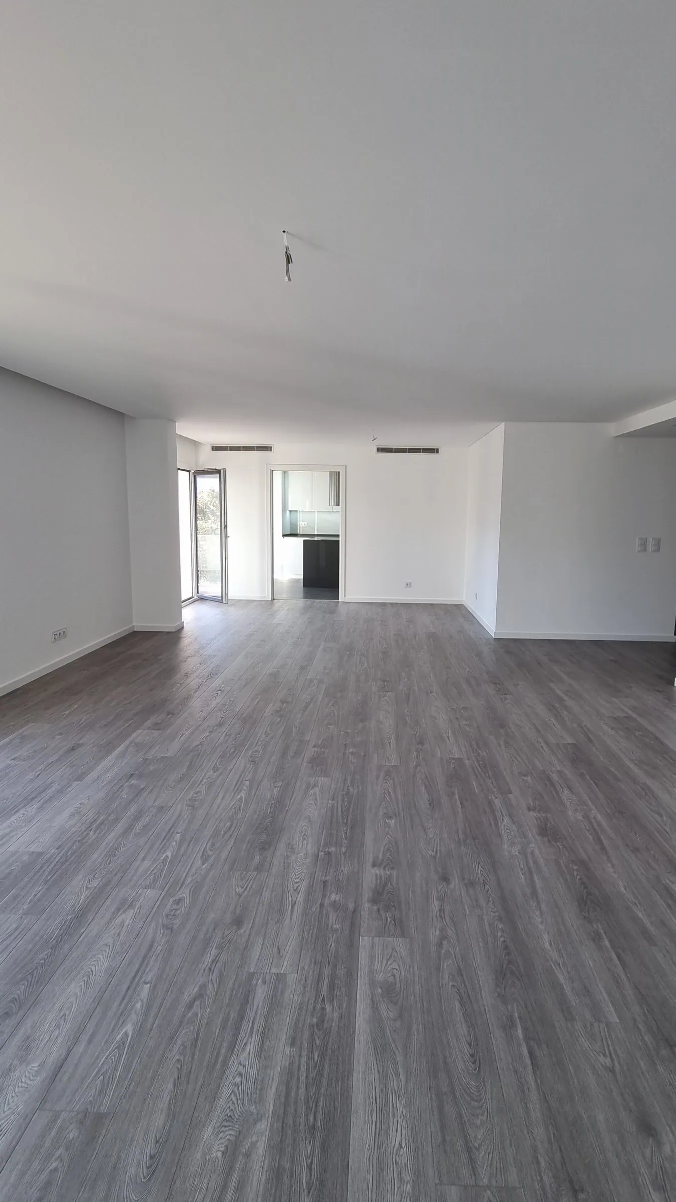A sala antes, vazia, com pavimento cinzento e a cozinha ao fundo.