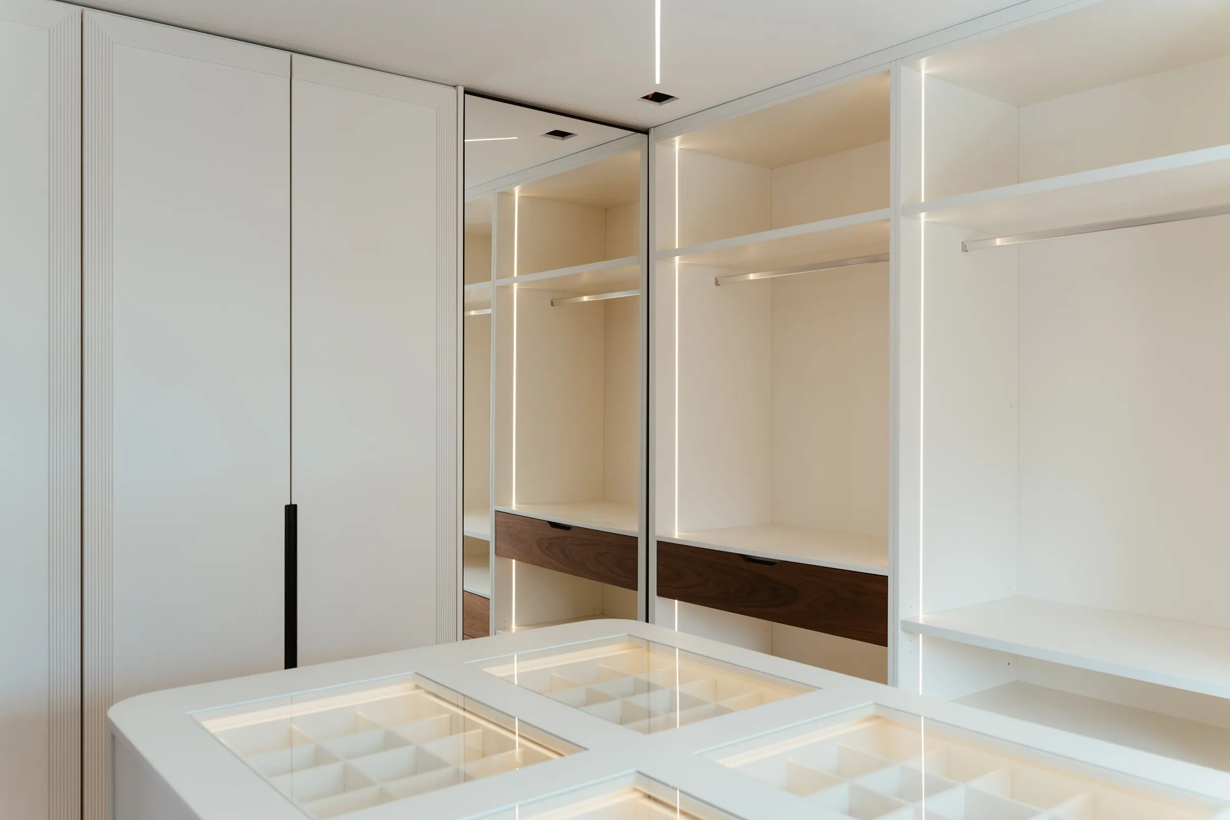 Closet com a ilha de tampo de vidro e os roupeiros abertos.