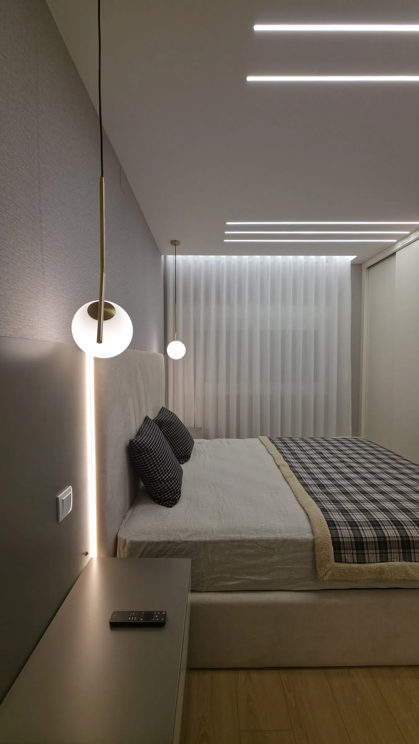 Quarto com cabeceira estofada, candeeiro suspenso e linhas de luz no teto.
