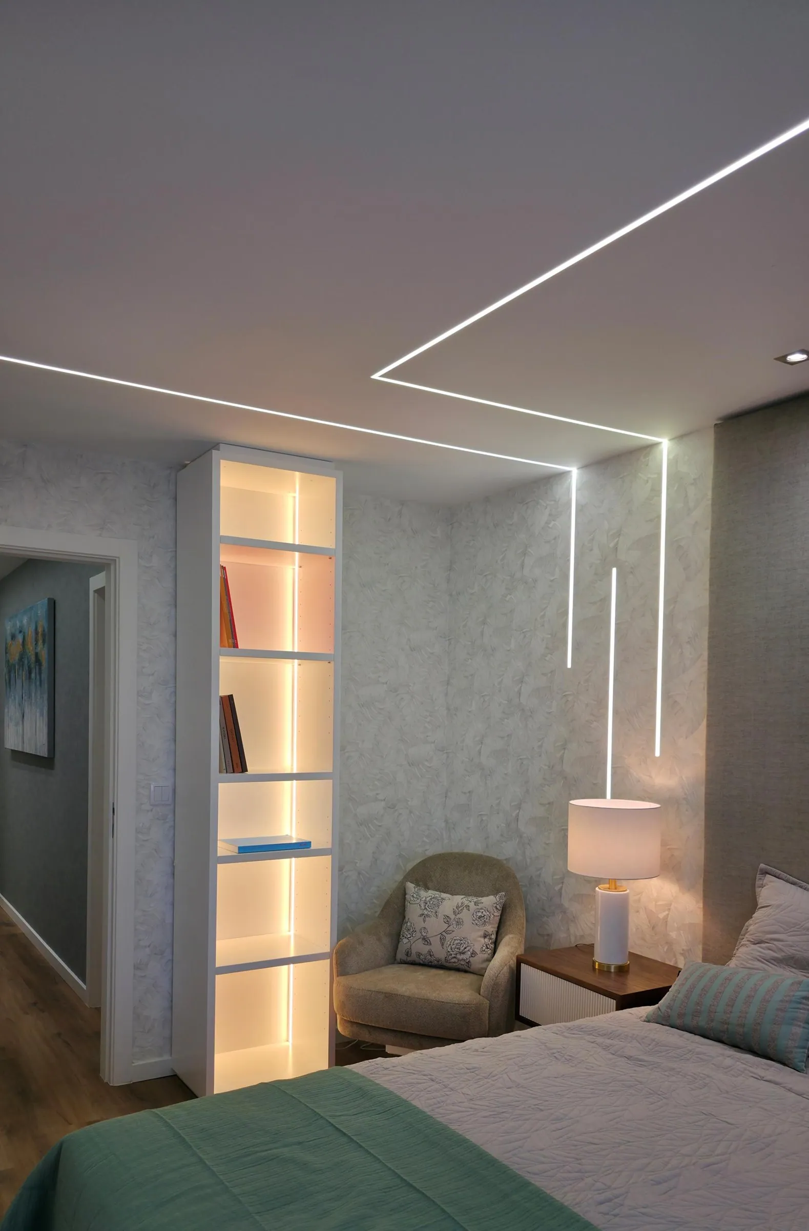 Quarto com estante iluminada e poltrona junto à janela.