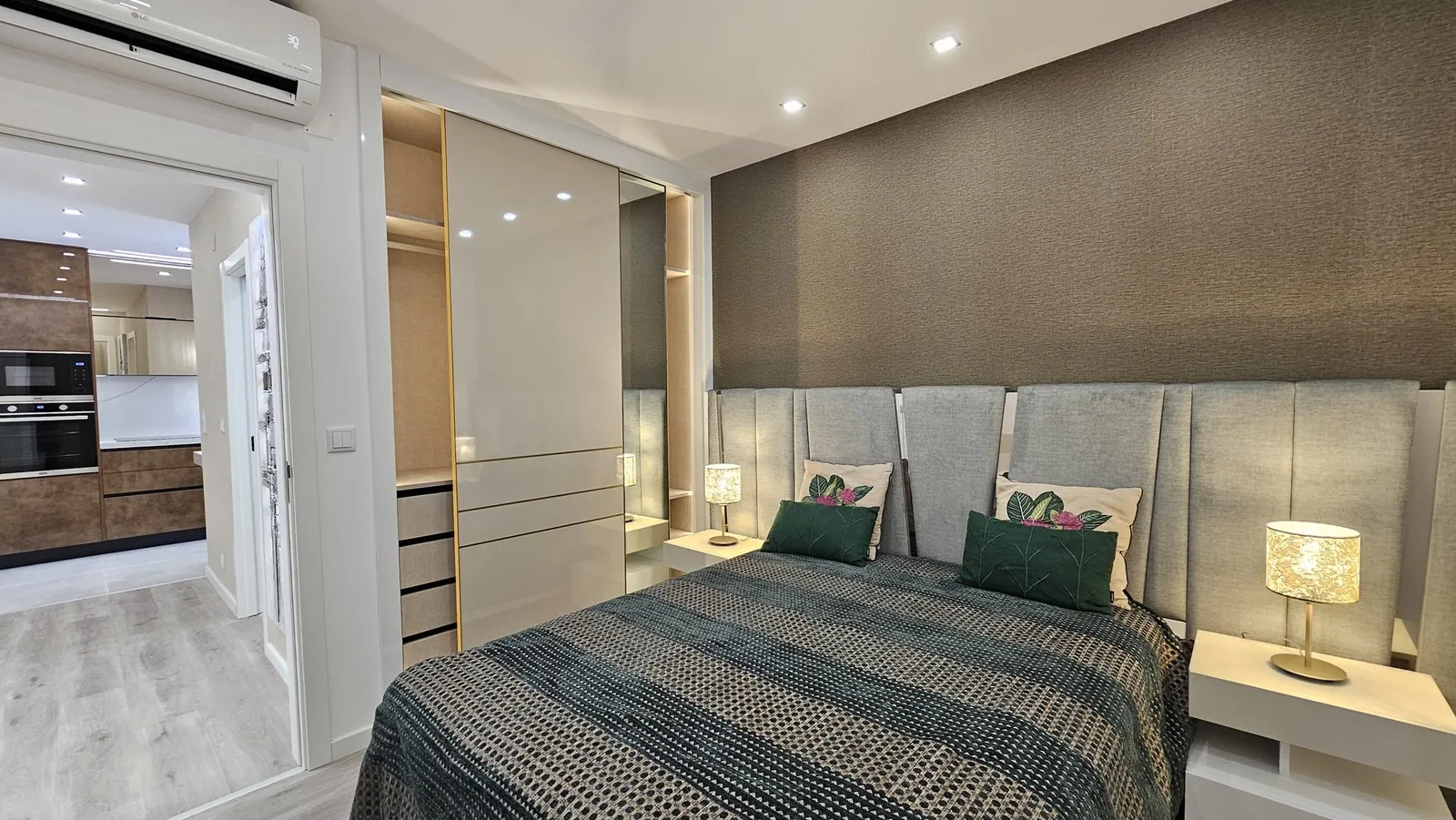 Quarto com cabeceira estofada e porta aberta para a cozinha em madeira.