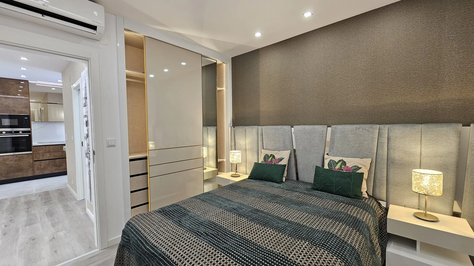 Quarto com cabeceira estofada e porta aberta para a cozinha em madeira.