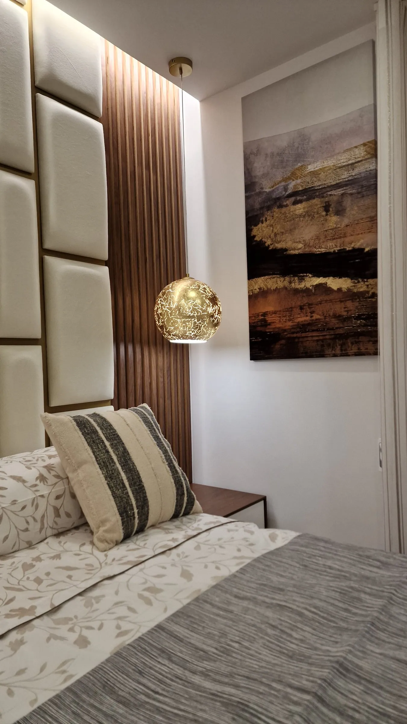 A cama, o ripado de madeira e um quadro de paisagem.